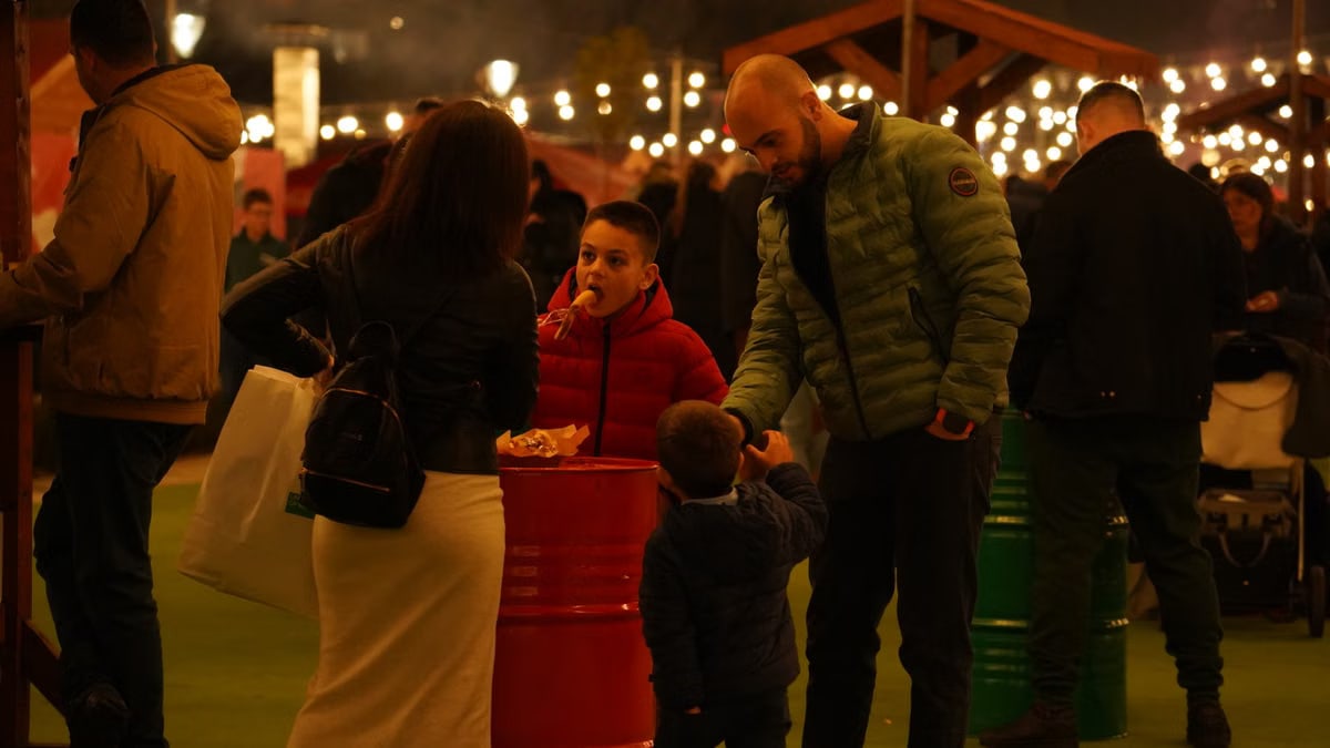 A family interacts at an evening street market with decorative lights and a bustling ambiance.